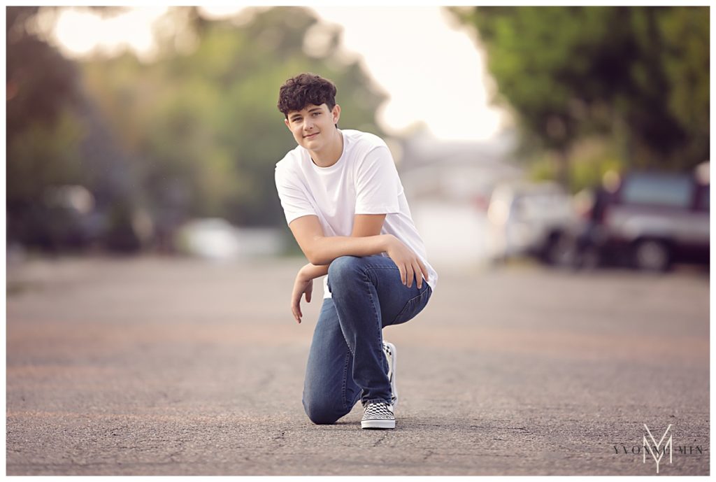 High school senior boy kneeling in a street during his high school photoshoot.