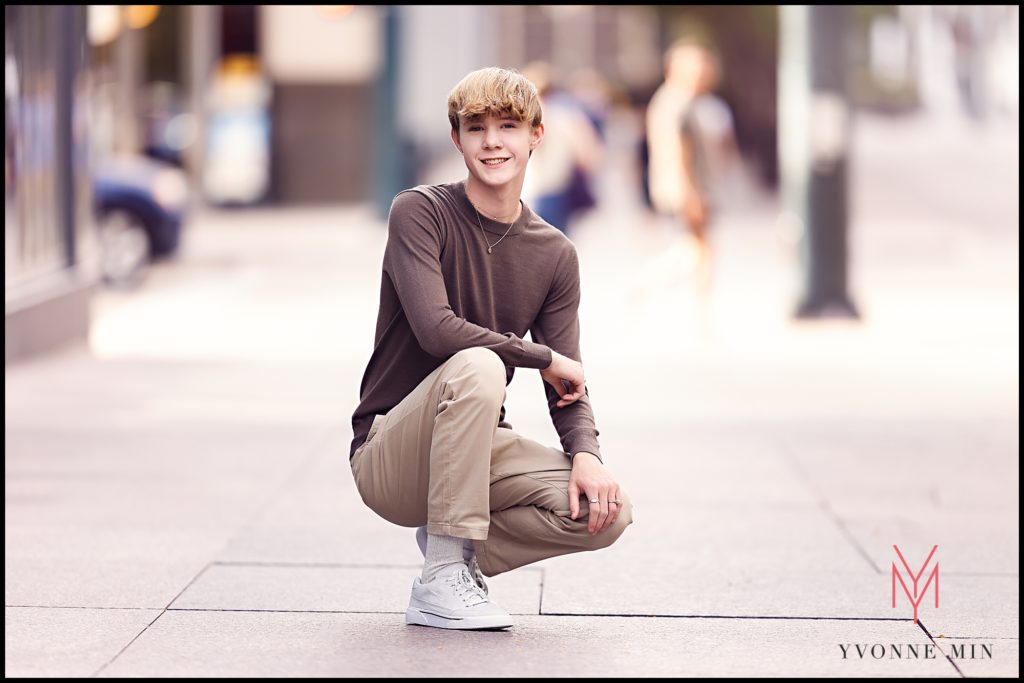 Shamus kneels down in the middle of a sidewalk in LoDo for one of his senior pictures.