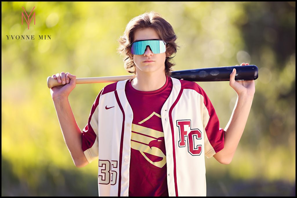 Ryan takes a senior photograph with a bat in a grassy field area of East Lake in Thornton, Colorado.