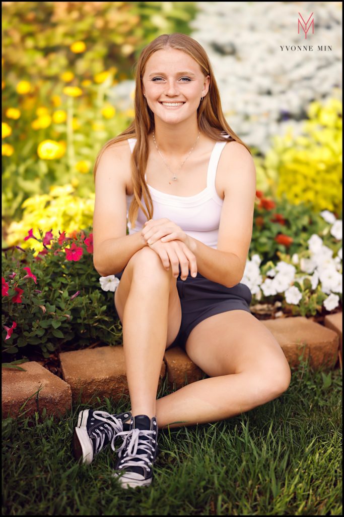 Taite poses for her senior photos in front of a large flower bed in the East Lake area of Thornton, Colorado.