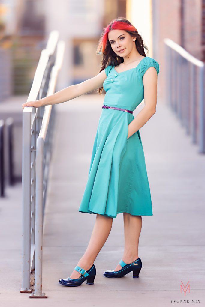 Grabbing onto a rail, a senior girl gets her senior pictures taken in downtown Denver with Yvonne Min.