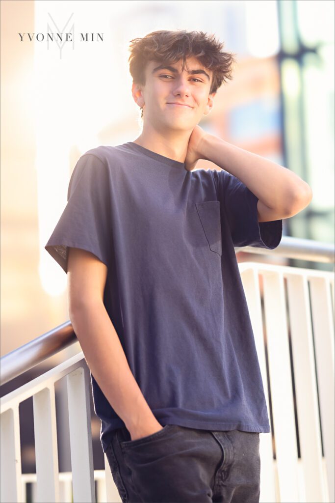 A high school senior boy poses in on stairs in a blue shirt during his senior photoshoot with Yvonne Min Photography in Denver.