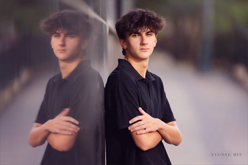 A teenage boy leans against a reflective black wall during his senior photoshoot in LoDo Denver.