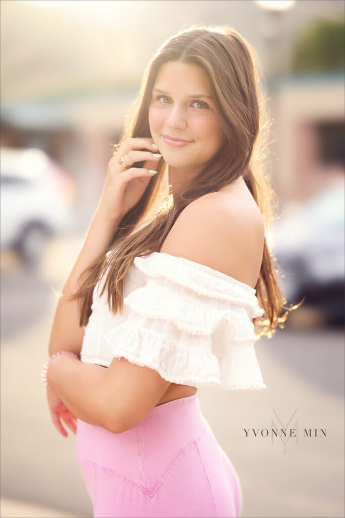 A high school senior girl poses in a white top and pink pants at her senior photoshoot in Golden, Colorado with Yvonne Min Photography.