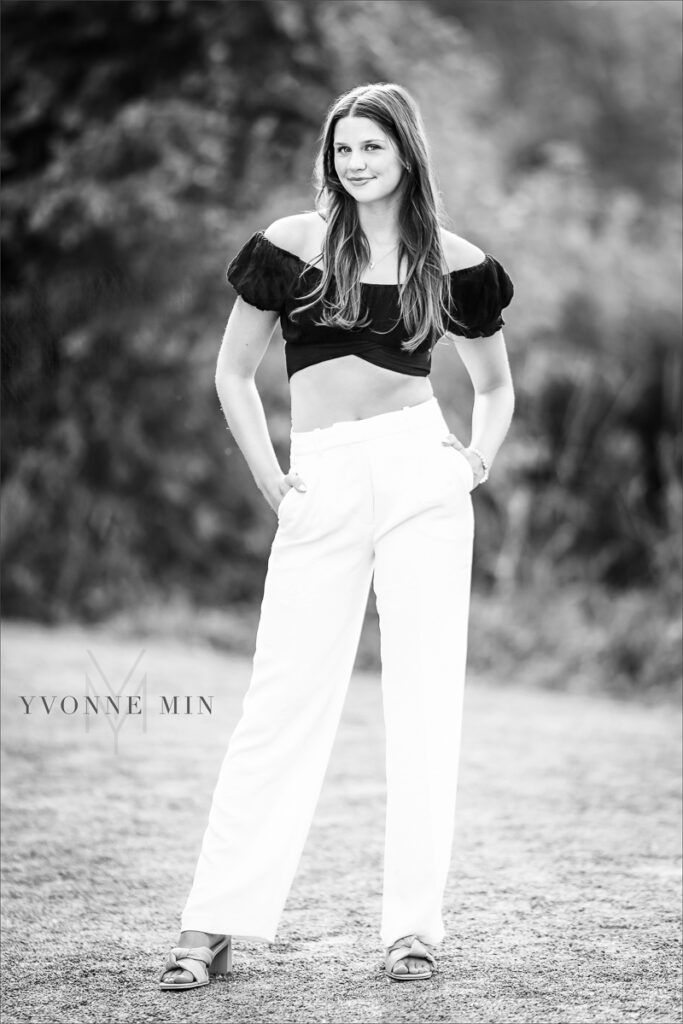 A high school senior girl poses in Golden, Colorado in white pants and a black top at her senior photoshoot.