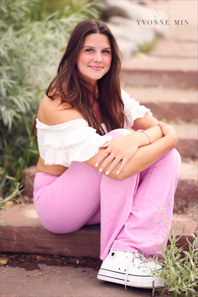 A high school senior girl sits on a stairs near the river walk in Golden, Colorado at her photoshoot with Yvonne Min Photography.