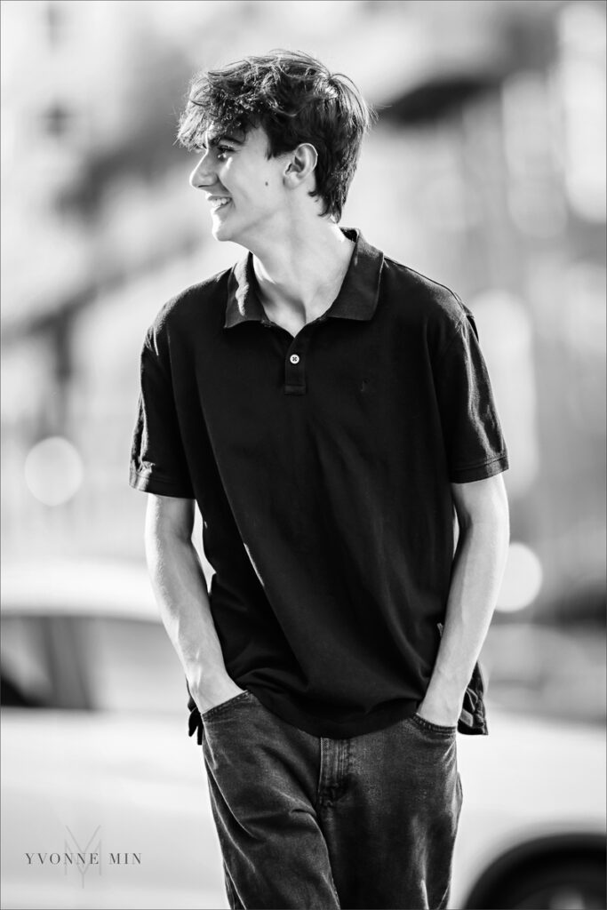 A black and white image of a high school senior boy walking in downtown Denver with Yvonne Min Photography.