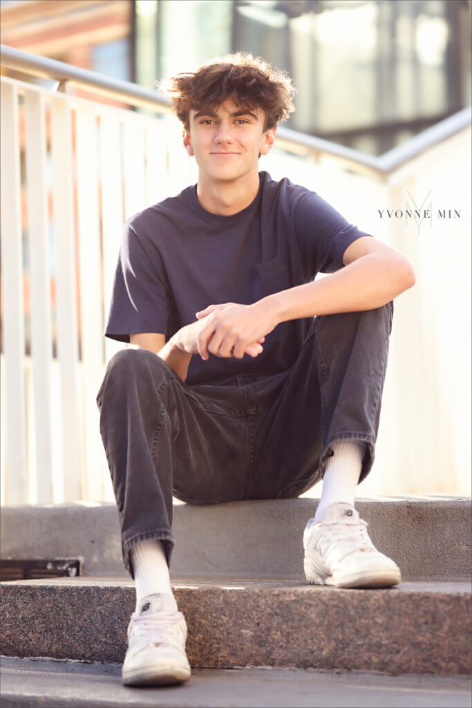 An Erie High School senior in Colorado sits on stairs in downtown Denver during his senior photoshoot with Yvonne Min Photography.