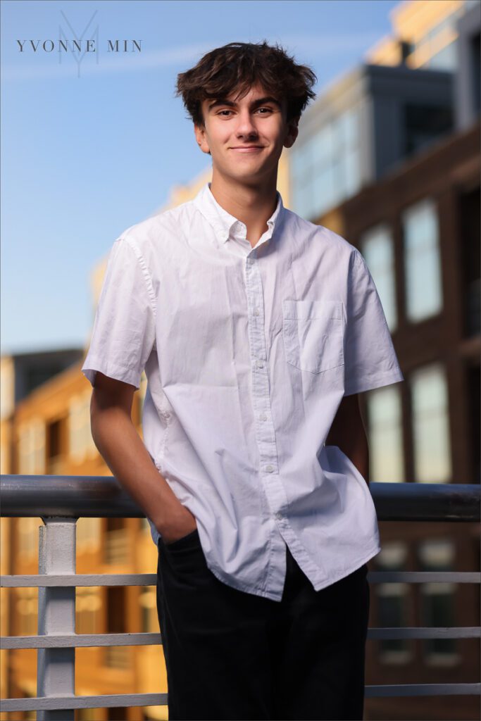 A teenage boy poses on the Millennium Bridge in downtown Denver in a white shirt during his senior photoshoot.