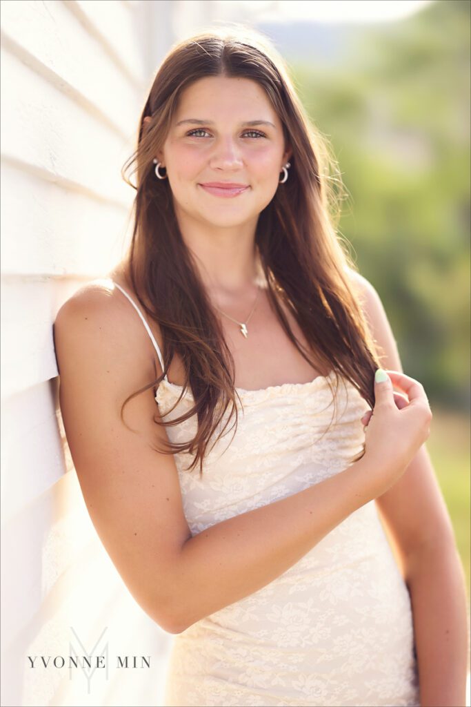 A high school senior girl leans on a wall in historic Golden, Colorado in a white dress at her senior photoshoot.