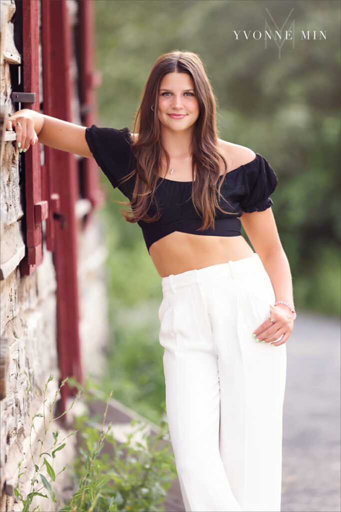 Senior high school girl leans on a wall in white pants during her senior photoshoot in Golden, Colorado.