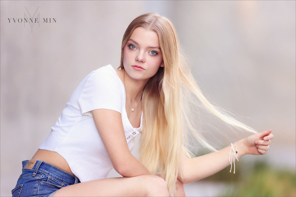 A high school senior girl poses in RiNo in Downtown Denver with her hair in her hand while being photographed by Yvonne Min Photography.