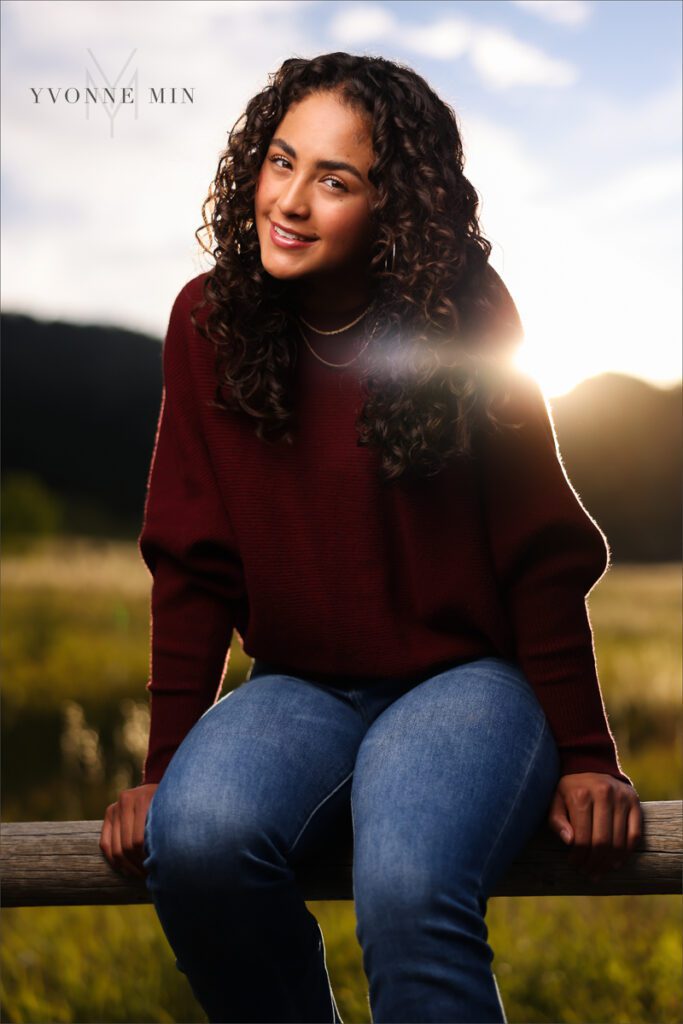 An off camera flash photo of a high school senior girl sitting on a fence in Chautauqua Park in Boulder, Colorado taken by Yvonne Min Photography.