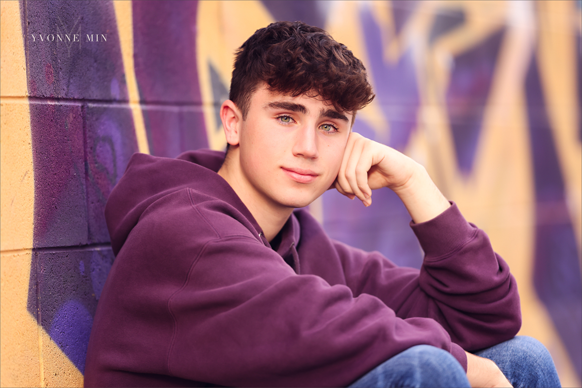 A high school senior basketball player from Stargate High School leans against a wall for his senior photos in RiNo Art District, Denver with Yvonne Min Photography.