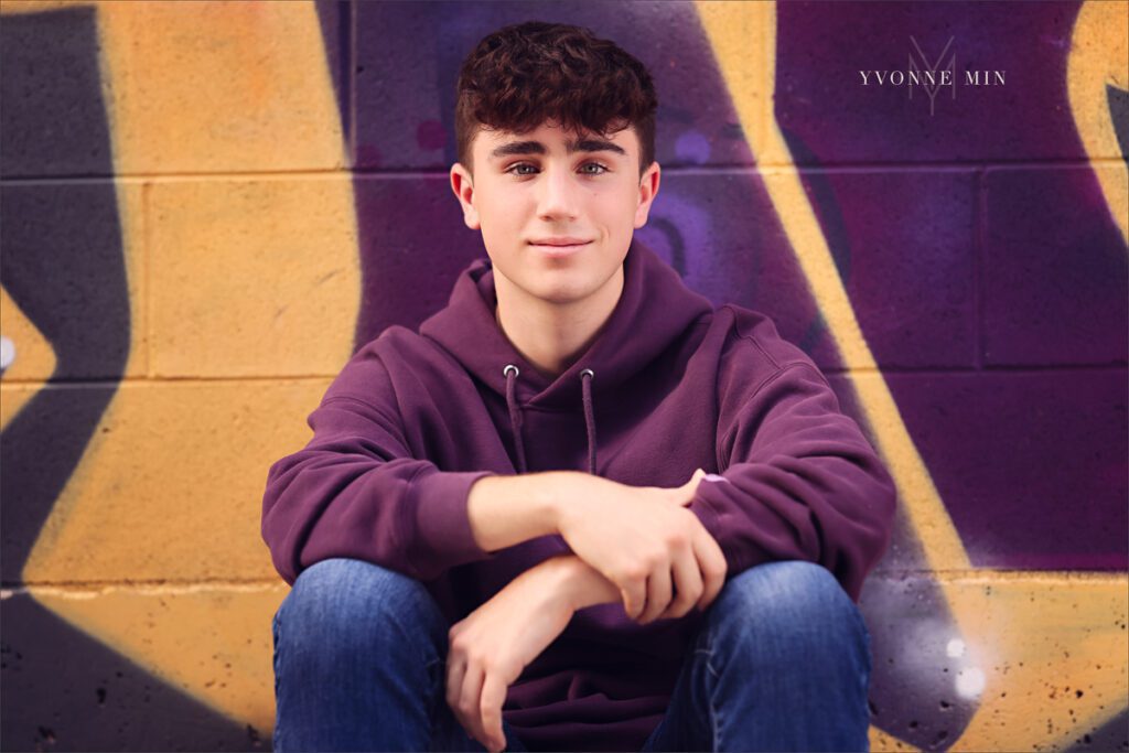 A high school senior basketball player from Stargate High School leans against a wall for his senior photos in RiNo Art District, Denver with Yvonne Min Photography.