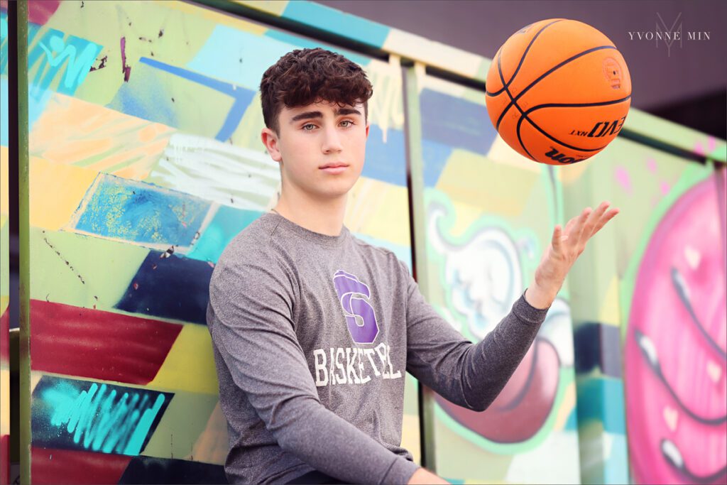 A senior boy from Stargate High School poses with his basketball during his senior photoshoot in the RiNo Art District in downtown Denver with Yvonne Min Photography.