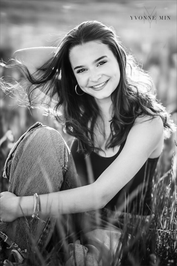 A black and white senior picture of a Stargate High School girl sitting in grass taken in Boulder, Colorado by Yvonne Min Photography.