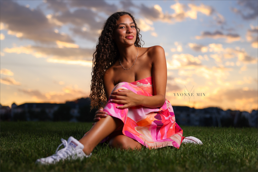A senior girl from East High School poses in a sundress in the grass at her senior photoshoot in downtown Denver with Yvonne Min Photography.