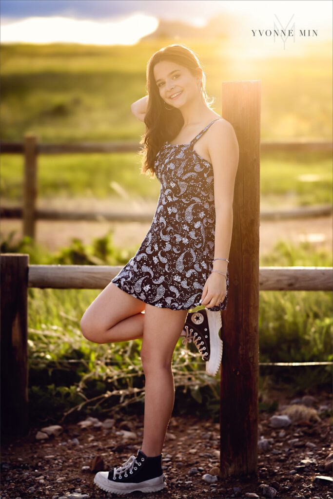 A senior picture of a Stargate High School girll leaning on a fence  at her senior photoshoot at Flatirons Vista outside Boulder, Colorado with Yvonne Min Photography.