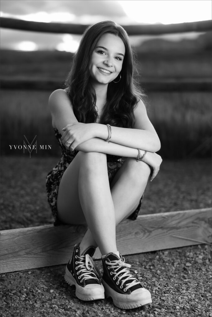 A black and white senior picture of a Stargate High School girl sits on a log at her senior photoshoot at Flatirons Vista outside Boulder, Colorado with Yvonne Min Photography.