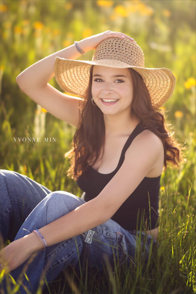 A Stargate High School senior girl sits in a field with yellow flowers at Flaitrons Vista outside Boulder, Colorado during her senior photoshoot with Yvonne Min Photography.