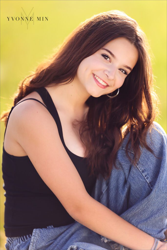 A Stargate High School senior girl sits in a field at Flaitrons Vista outside Boulder, Colorado during her senior photoshoot with Yvonne Min Photography.