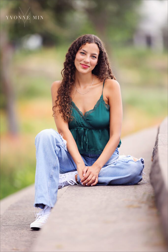 A senior picture of a girl sitting on a sidewalk from East High School taken in Lodo, Denver by Yvonne Min Photography near Confluence Park.
