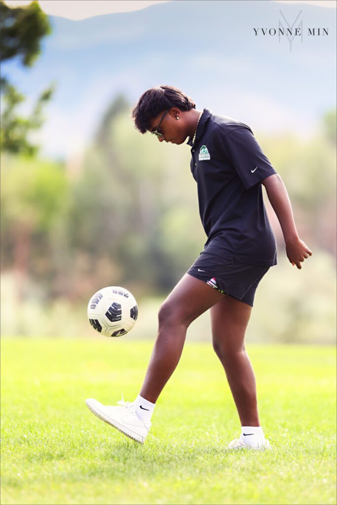 A high school senior picture of a Stargate student kicking a soccer ball at his senior photoshoot at Purple Park in Arvada with Yvonne Min Photography.