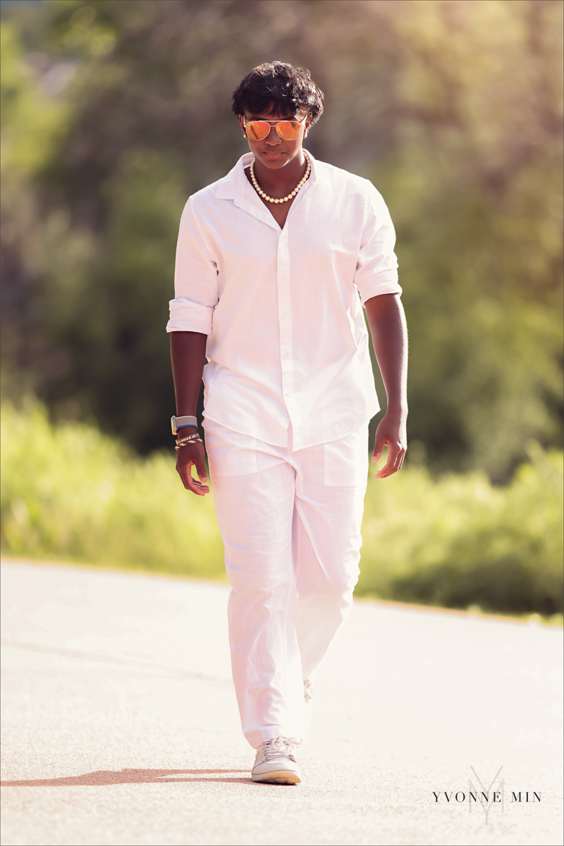 A high school senior picture of a Stargate student walking on a sidewalk in all white at his senior photoshoot at Purple Park in Arvada with Yvonne Min Photography.