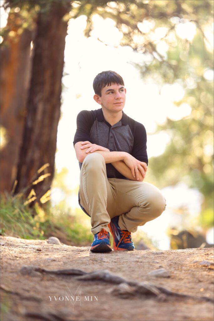 A senior picture of a Stargate High School senior boy kneeling in a gray t-shirt taken in the mountains above Boulder, Colorado by Yvonne Min Photography.