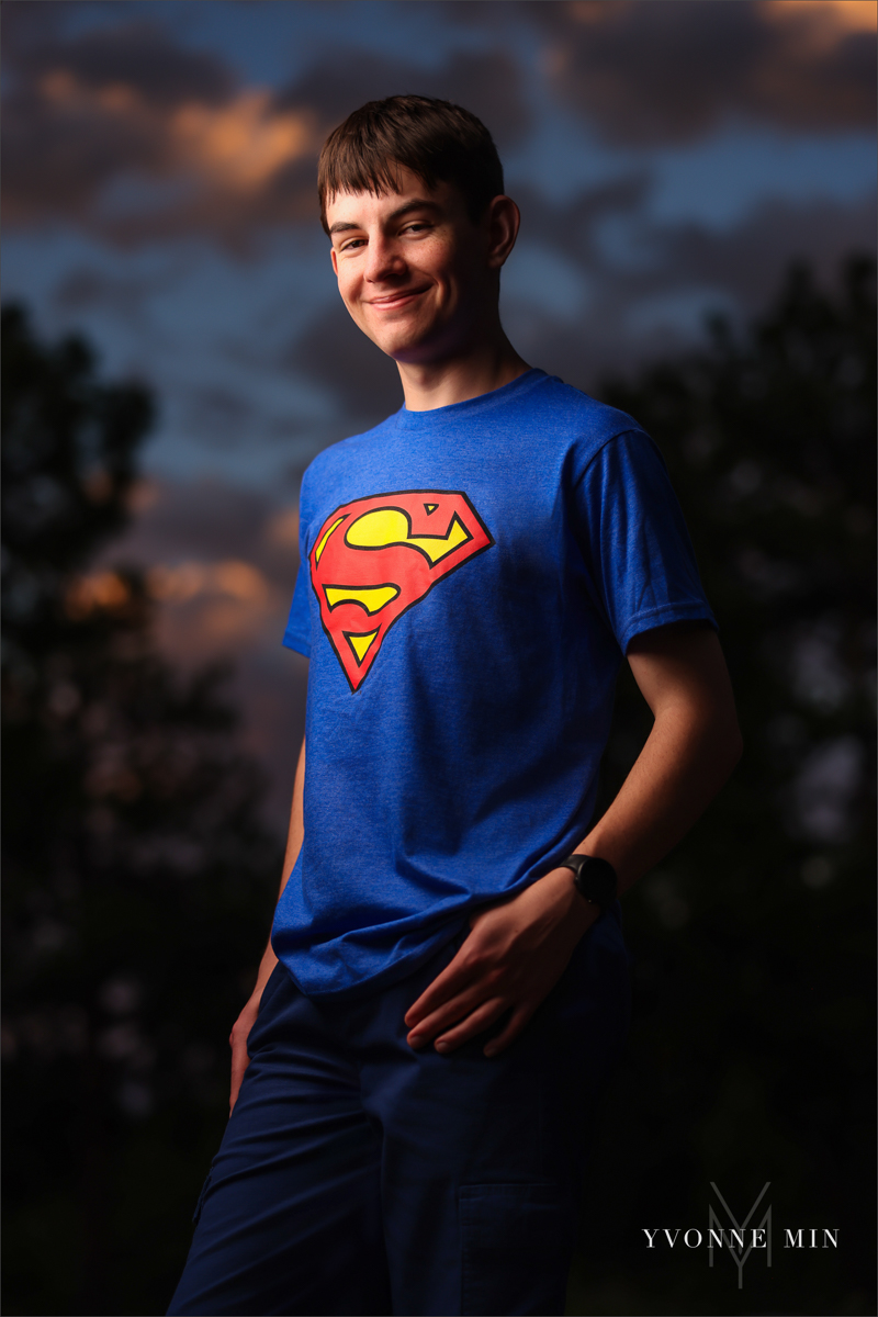 A senior photo of a Stargate High School boy in a superman t-shirt with a sunset in the mountains taken by Yvonne Min Photography in Boulder, Colorado.