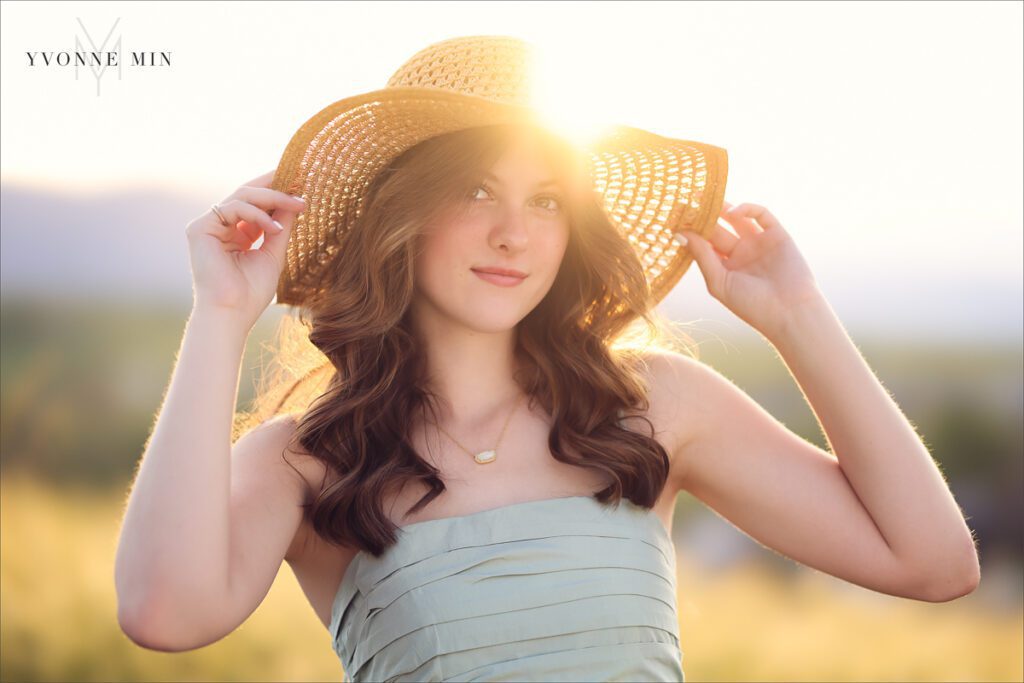 A Stargate High School senior girl poses in a hat for her senior pictures photoshoot in the grassy area of Purple Park, Superior, Colorado taken by Yvonne Min Photography.