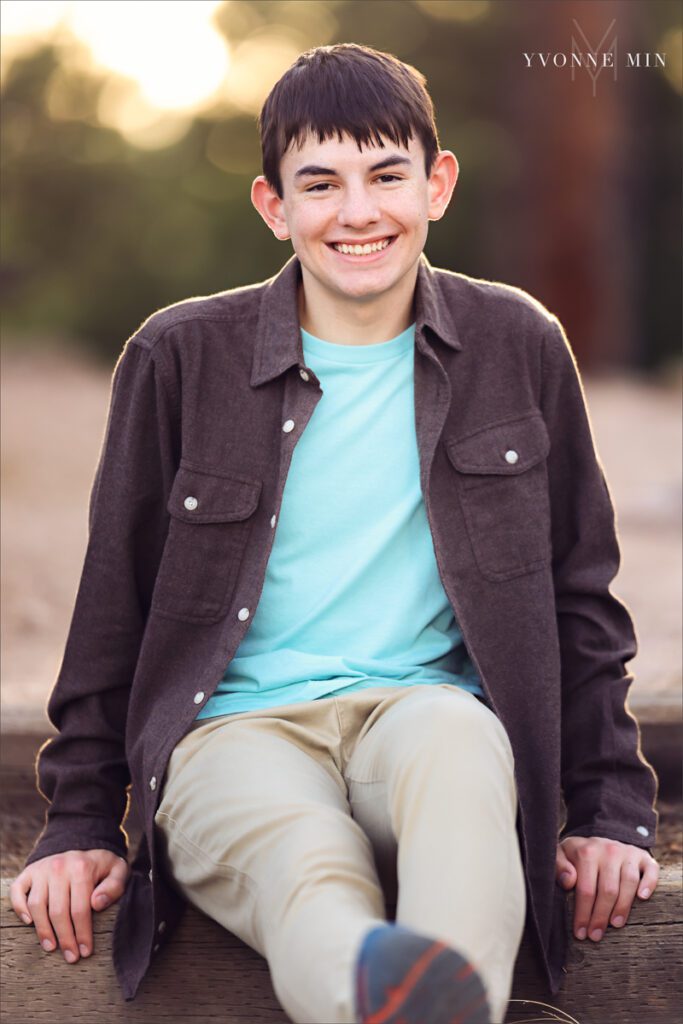 A senior boy from Stargate High School poses on a trail at Chautauqua Park in Boulder, Colorado in a brown jacket with Yvonne Min Photography.