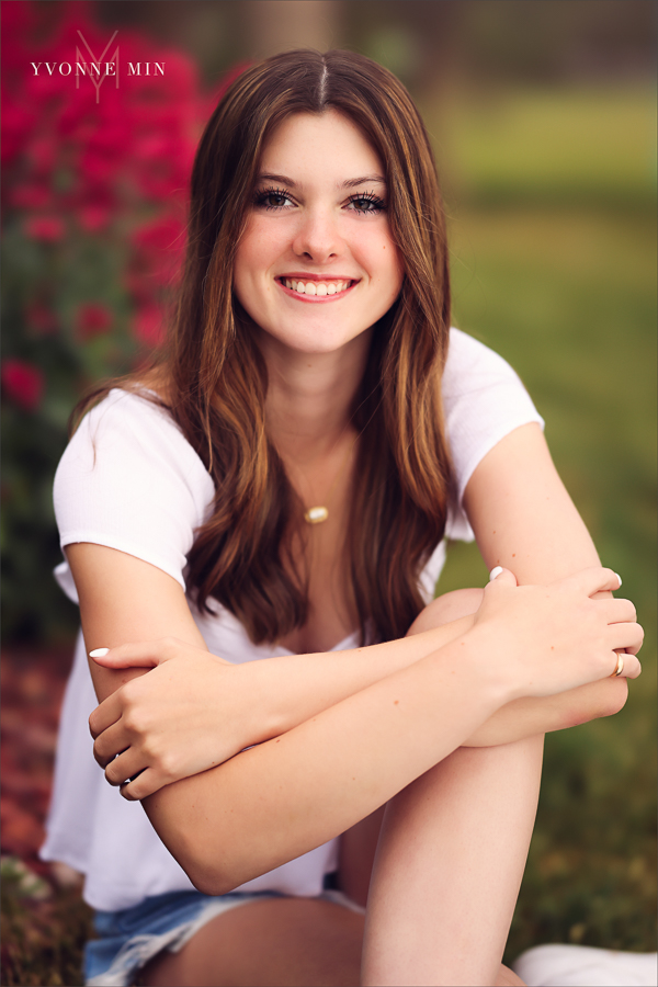 A Stargate High School senior girl poses for her senior pictures photoshoot in front of red flowers in Purple Park, Superior, Colorado taken by Yvonne Min Photography.