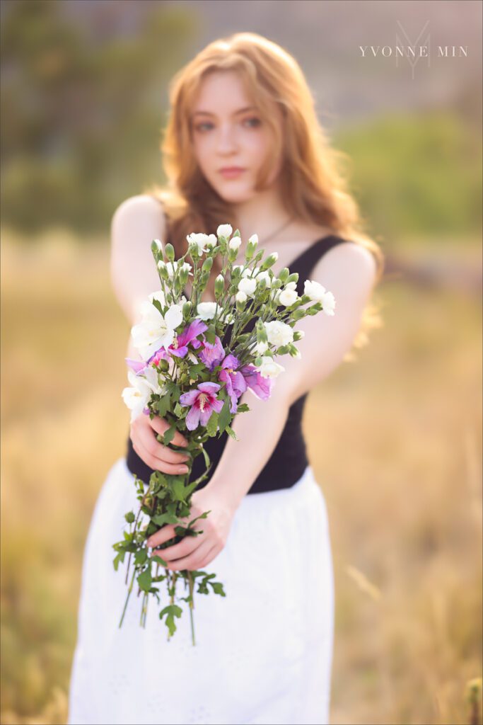 A high school senior girl from Stargate poses with a bouquet of flowers at her senior photoshoot with Yvonne Min Photography at South Mesa Trailhead.