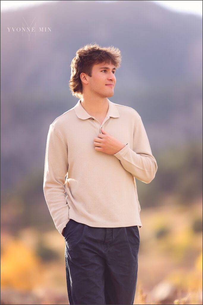 A senior boy wearing a cream sweater walks in a field during his senior photoshoot at South Mesa in Boulder with Yvonne Min Photography.