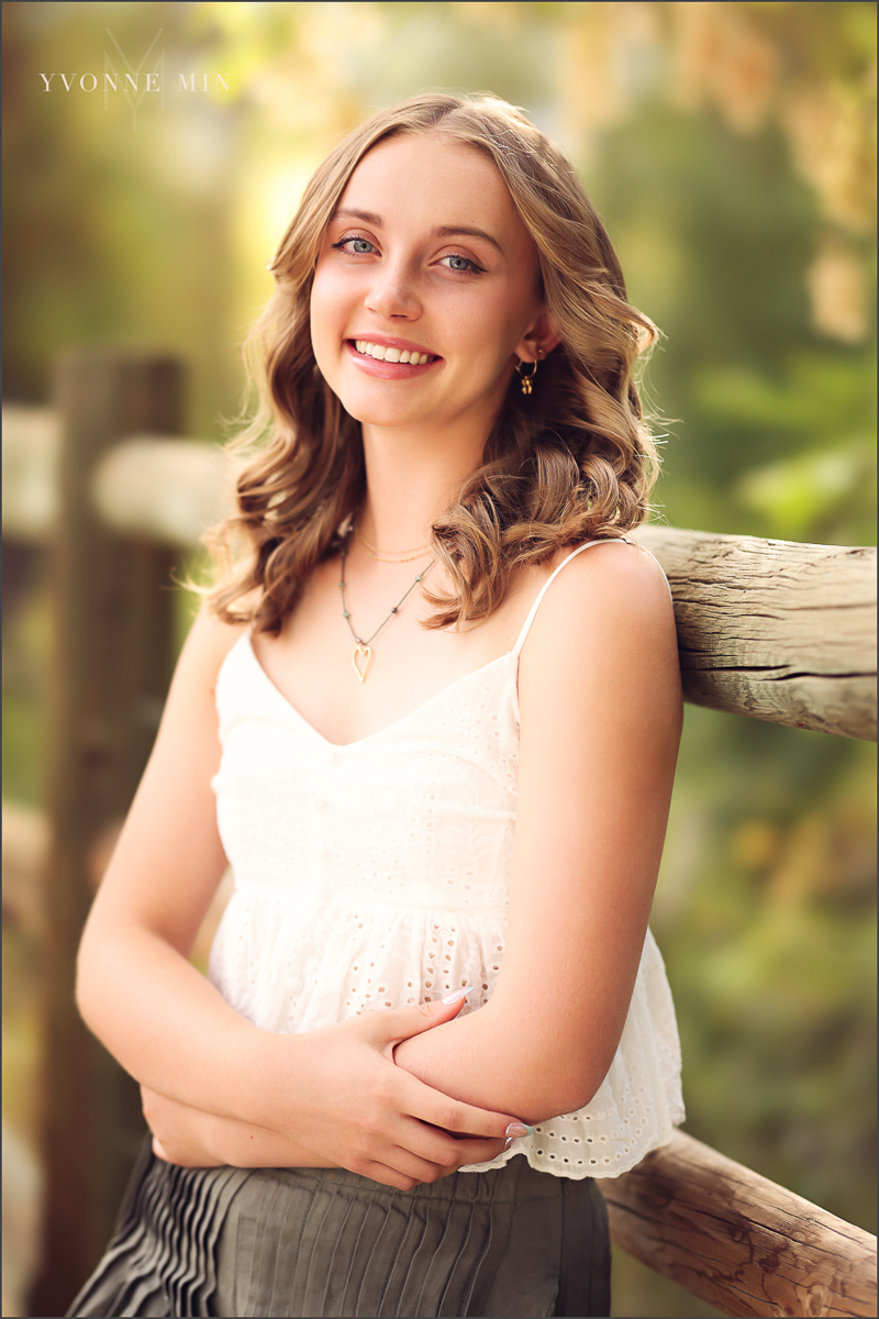 A high school senior girl poses against a fence at her senior photoshoot at South Mesa Trailhead outside Boulder with Yvonne Min Photography.