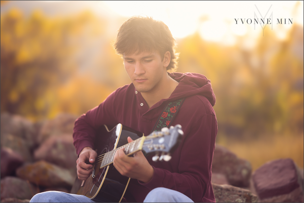 A senior guy from Nothfield High Schools plays a guitar during his senior photoshoot at South Mesa Trailhead outside Boulder with Yvonne Min Photography.