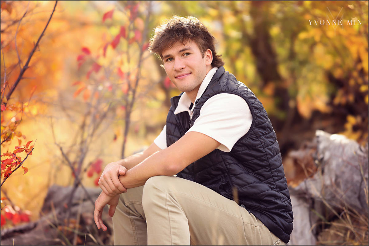 A high school senior boy from Northfield High School sits on a log during his photoshoot at South Mesa Trailhead with Yvonne Min Photography.