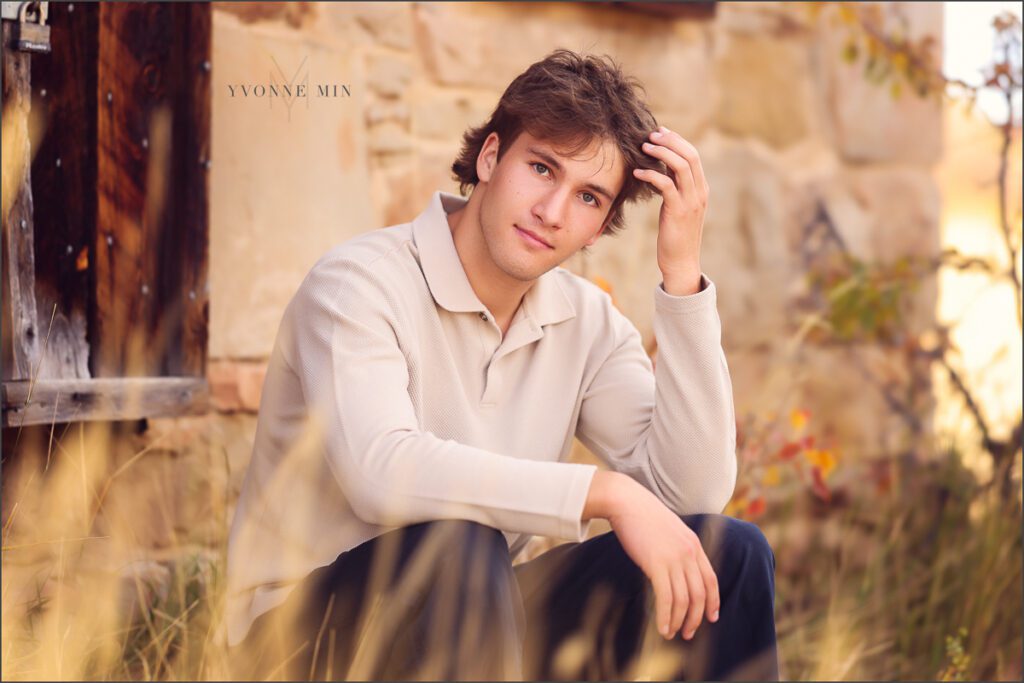 A high school senior boy sits on a step outside a historical building during his photoshoot at South Mesa Trailhead with Yvonne Min Photography.