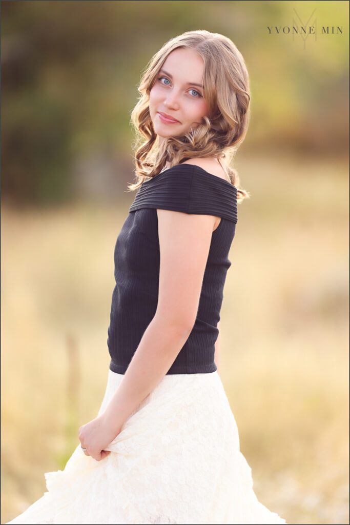 A high school senior girl from Jefferson Academy poses in a field at her senior photoshoot at South Mesa Trailhead outside Boulder with Yvonne Min Photography.