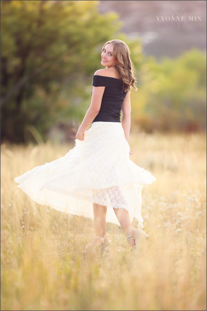 A high school senior girl from Jefferson Academy poses in a field at her senior photoshoot at South Mesa Trailhead outside Boulder with Yvonne Min Photography.