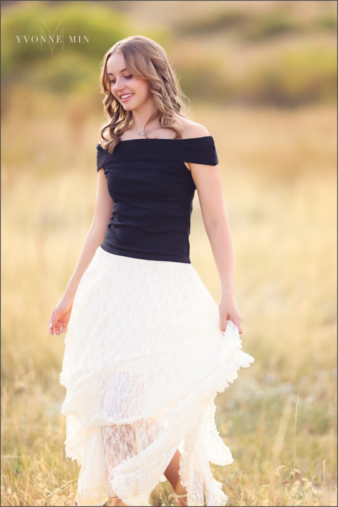 A high school senior girl from Jefferson Academy poses in a field at her senior photoshoot at South Mesa Trailhead outside Boulder with Yvonne Min Photography.