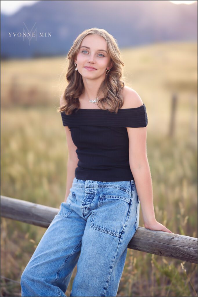 A high school senior girl from Jefferson Academy poses on a fence at her senior photoshoot with Yvonne Min Photography at Flatirons Vista outside Boulder.