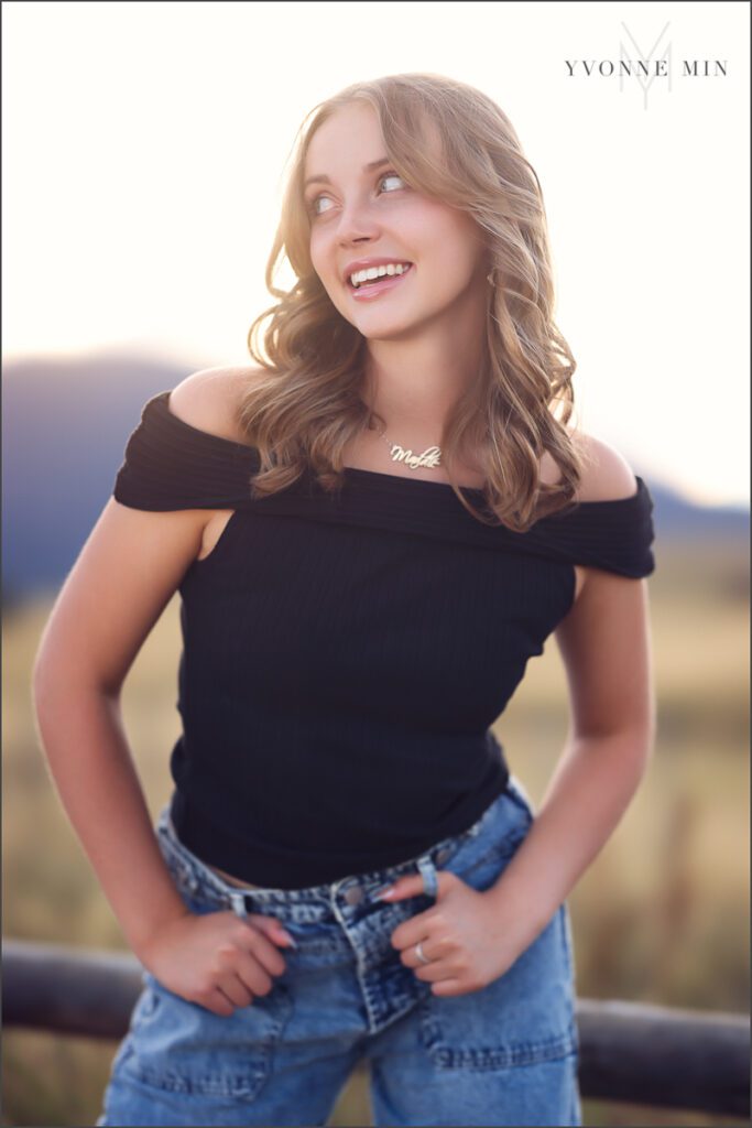 A high school senior girl from Jefferson Academy poses on a fence at her senior photoshoot with Yvonne Min Photography at Flatirons Vista outside Boulder.