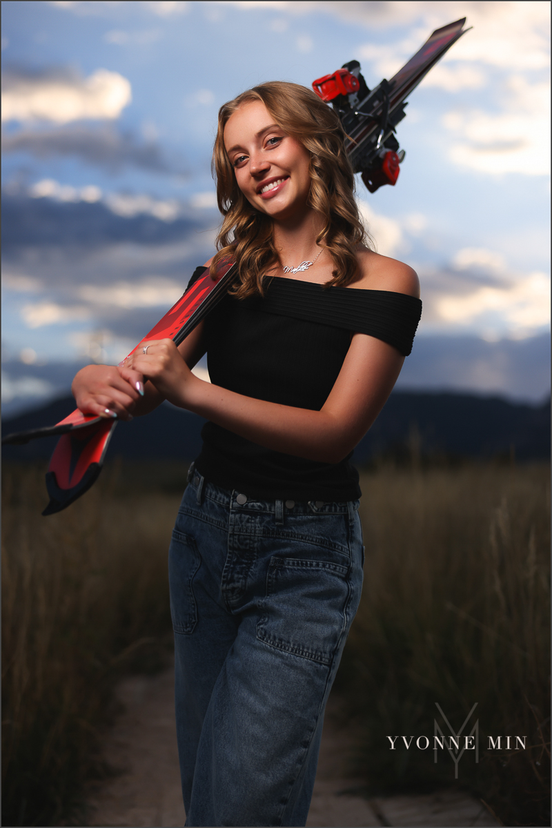 An OCF (off camera flash)senior photo of a girl holding skis from Jefferson Academy at her senior photoshoot with Yvonne Min Photography at Flatirons Vista Trailhead outside Boulder, Colorado.