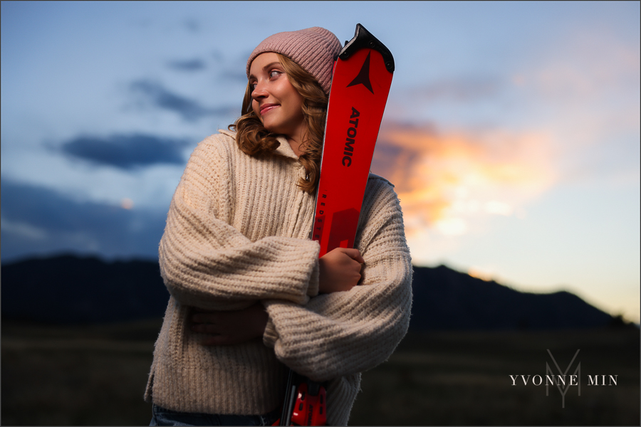 An OCF (off camera flash)senior photo of a girl holding skis from Jefferson Academy at her senior photoshoot with Yvonne Min Photography at Flatirons Vista Trailhead outside Boulder, Colorado.