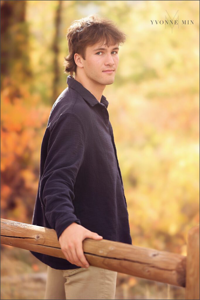 A senior boy poses on a fence at his senior photoshoot at South Mesa in Boulder with Yvonne Min Photography.