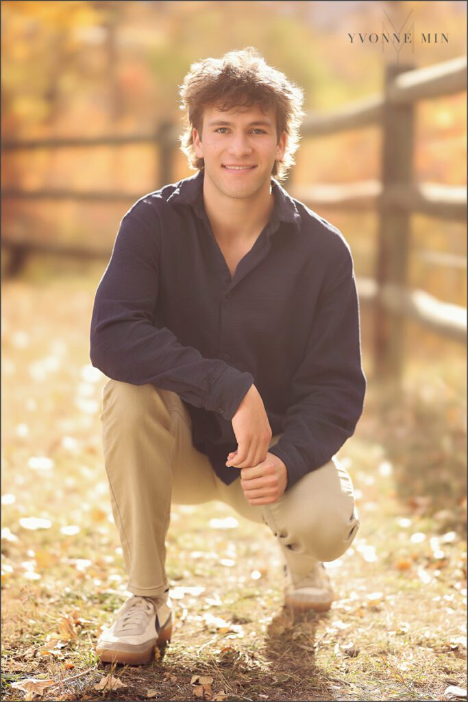 A senior boy from Northfield High School squats in the sunset light at his senior photoshoot with Yvonne Min Photography.