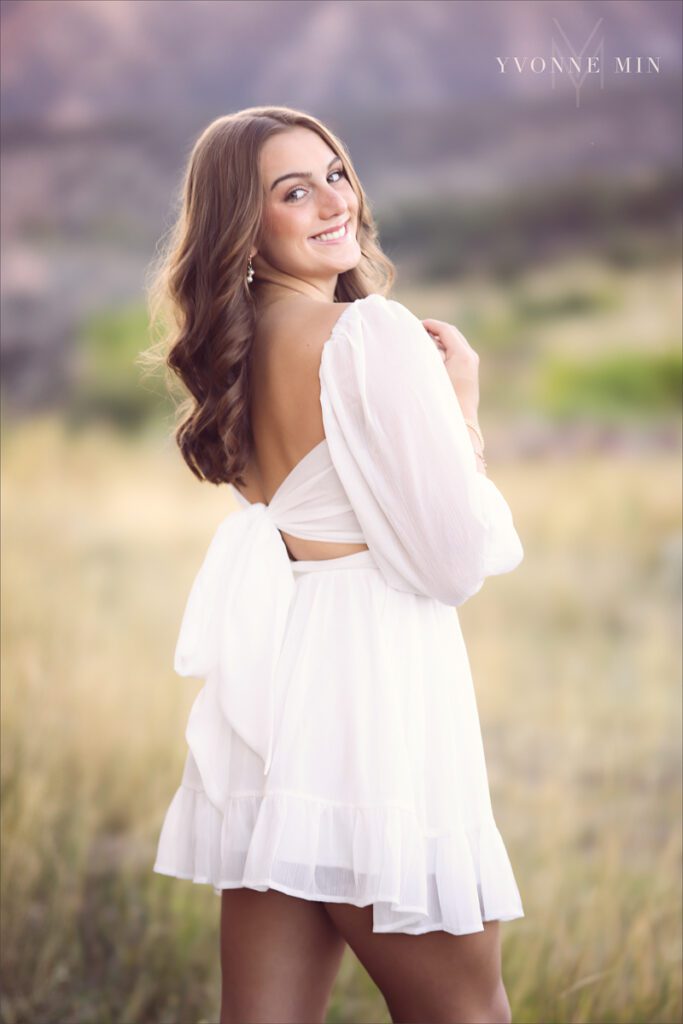 A senior girl from Legacy High School poses in a white dress at her senior photoshoot with Yvonne Min Photography at South Mesa Trailhead near Boulder, Colorado.